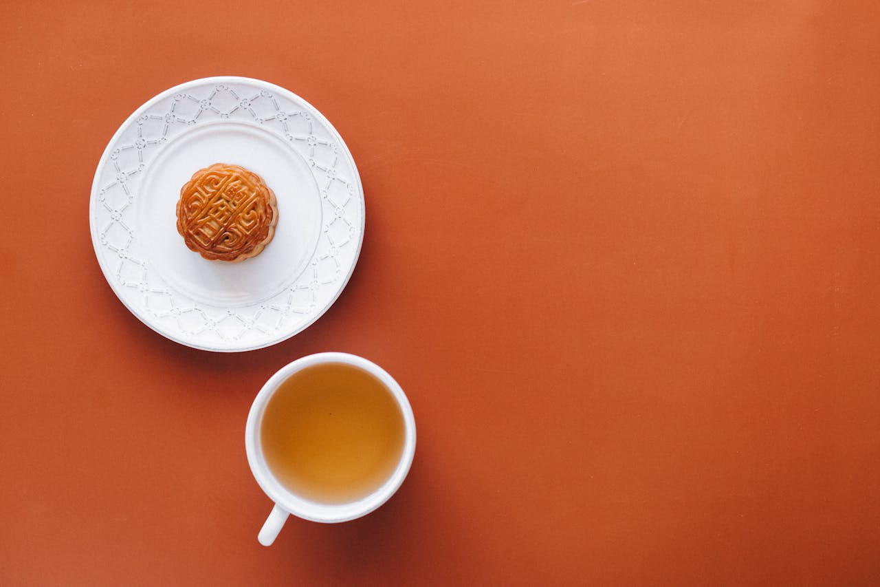 Overhead view of a traditional mooncake and tea on a vibrant orange background, perfect for cultural and culinary themes.